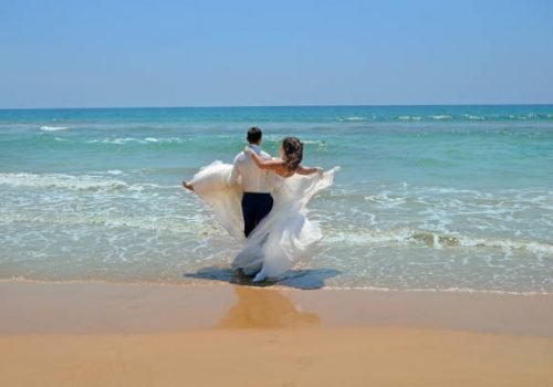 the groom in a suit carries on his hands the bride in a wedding dress in the waters of the Indian Ocean. Wedding and honeymoon in the tropics on the island of Sri Lanka
